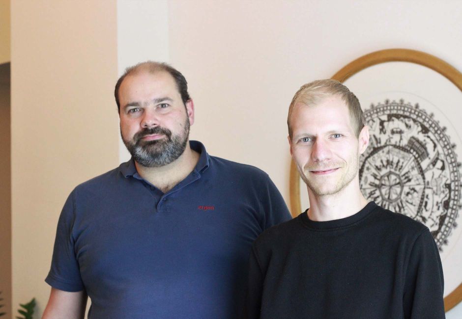 Noah und Kevin befinden sich im Eingangsbereich von Ergon. Hinter ihnen ist ein Bild zu sehen, das aus einem runden Scherenschnitt besteht. Der Scherenschnitt bildet die Geschichte von Ergon ab. Noah und Kevin befinden sich im Eingangsbereich von Ergon. Hinter ihnen ist ein Bild zu sehen, das aus einem runden Scherenschnitt besteht. Der Scherenschnitt bildet die Geschichte von Ergon ab.